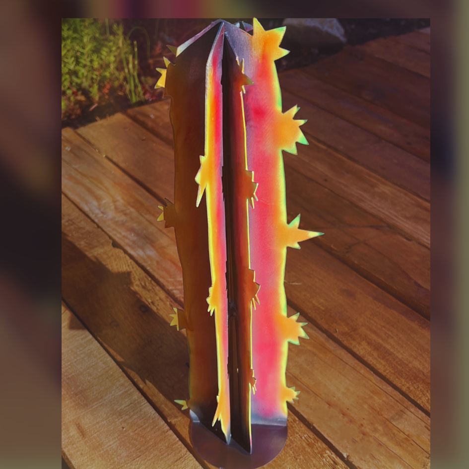 Metal Cactus art on a wooden floor. Cactus has spkes, and is colored with pink, yellow green, and purple