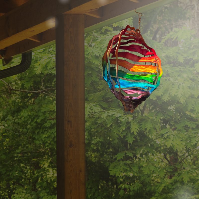 Rainbow colored wind spinner handmade art, hanging from pergola, with oak leaves background