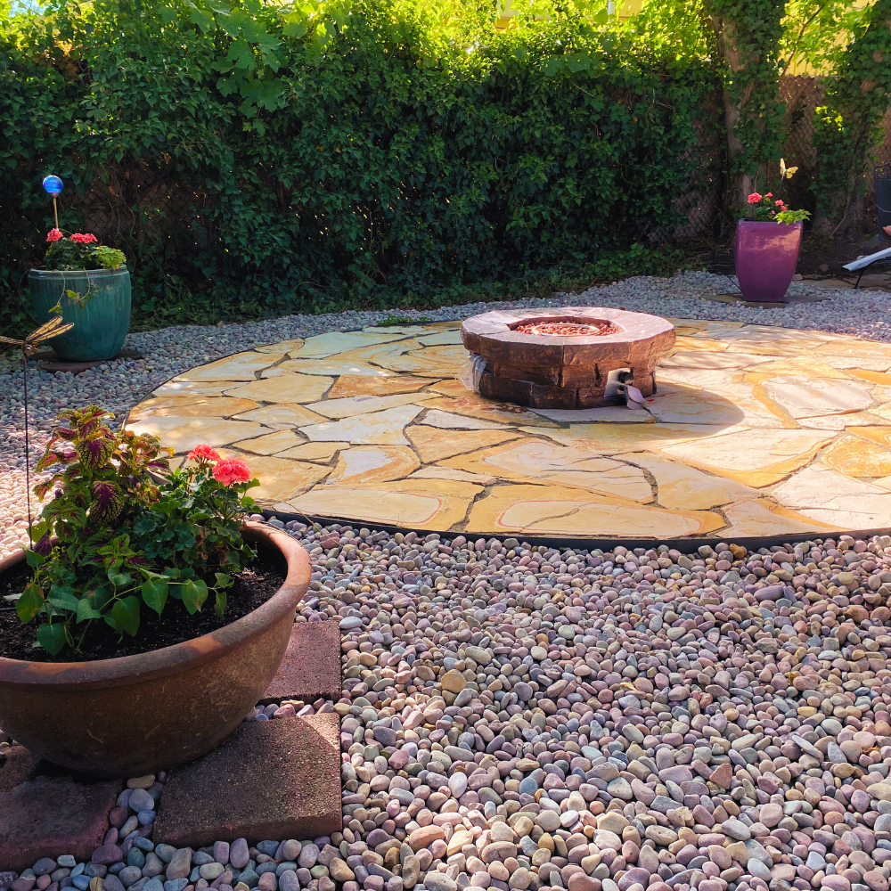 Flagstone patio in a round shape, in a landscaping scene, with custom fire pit, planter pots with flowers. Rainbow pebbles, ivy 