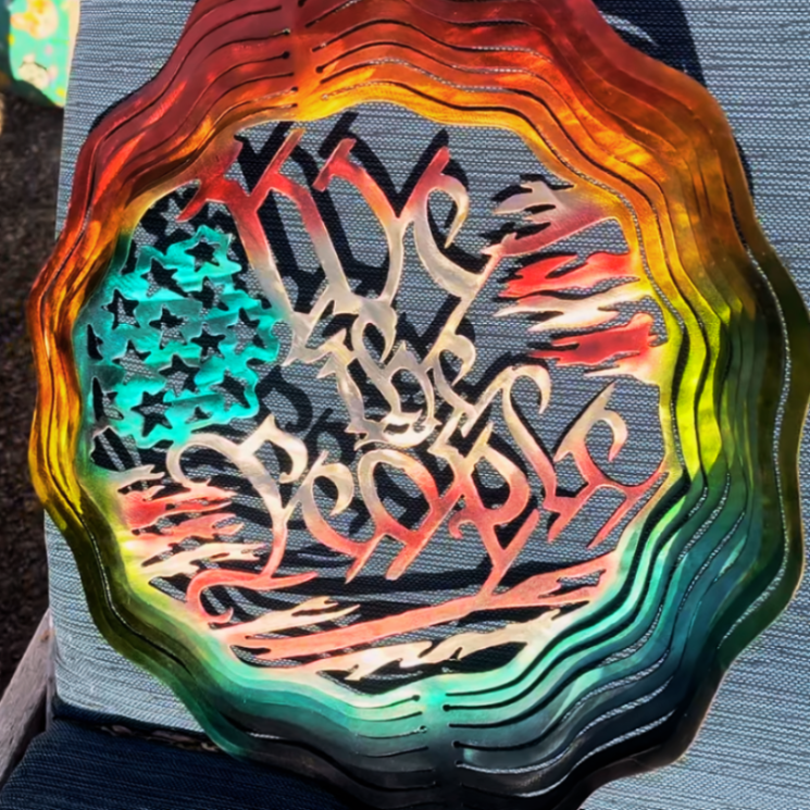 Made of steel, painted with rainbow gradient colors, with text in the middle that says "We The People". 