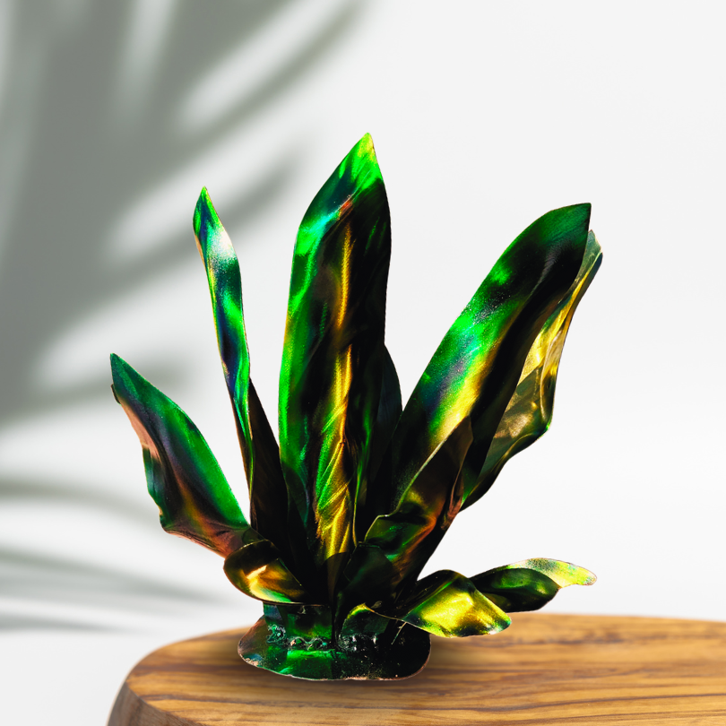 Green, Yellow, Gold, Metal garden art agave, on a round piece of wood, with a plant shadow in the background. 