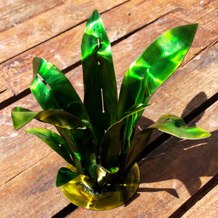 Spiky Desert Plant made of metal, displayed on a wooden background, with green and a hint of yellow on the leaves, a yellow base, welded metal art for the garden or outdoor spaces or indoor. Fake metal plant that catches sunlight 
